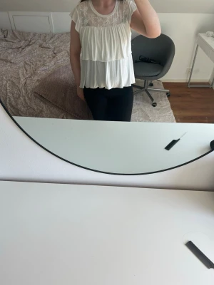 Vit volangblus med spetsdetaljer - Söt vit blus med volanger och spets upptill. Blusen är ärmlös och har en luftig, flowy passform som känns både romantisk och trendig. Perfekt att styla med jeans eller kjol för en fräsch look.