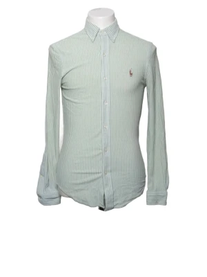 Randig skjorta från Ralph Lauren - Snygg ljusgrön och vit randig skjorta från Ralph Lauren med klassisk krage och knappar framtill. Skjortan har lång ärm och broderad logga på bröstet. Perfekt för en stilren look.
