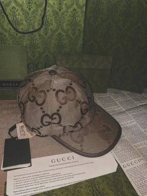 Brun keps från Gucci med GG-mönster - Snygg brun keps från Gucci med det klassiska GG-monogrammet över hela kepsen. Kepsen har böjd skärm och justerbar rem baktill. Tillverkad i canvasmaterial med exklusiv känsla och tydliga logodetaljer. Alla tillbehör med följer förutom kvitton 