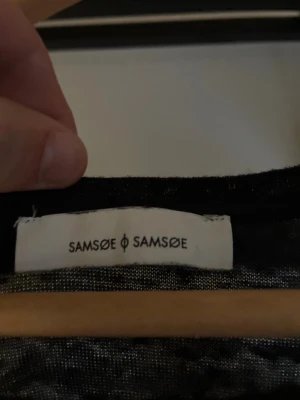 Svart långärmad tröja Samsøe Samsøe - En svart långärmad tröja från Samsøe Samsøe med rund halsringning. Tröjan har en enkel och stilren design, perfekt för lager på lager och passar till det mesta. Materialet ser ut att vara mjukt och tunt, vilket gör den skön att bära.