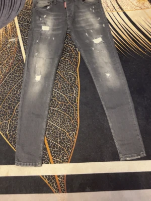 Grå slitna jeans från Dsquared2 - Säljer ett par grå skinny jeans från Dsquared2 med slitningar och distressed detaljer på både fram- och baksida. Jeansen har klassisk femficksmodell, bälteshällor och knappgylf. Perfekta för dig som gillar en edgy streetstyle.