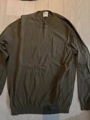 Olivgrön tröja från Zara - Snygg olivgrön tröja från Zara med rund halsringning och långa ärmar. Tröjan är tunnstickad och har ribbade muddar vid ärmslut och nederkant. Perfekt för lager-på-lager och enkel att matcha med olika outfits.