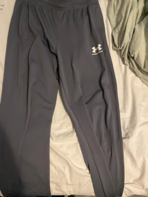 Grå mjukisbyxor från Under Armour - Snygga grå mjukisbyxor från Under Armour med elastisk midja och vit logga på låret. Byxorna har en avslappnad passform och är tillverkade i ett mjukt och bekvämt material som passar perfekt för chill eller träning. Pris kan diskuteras!