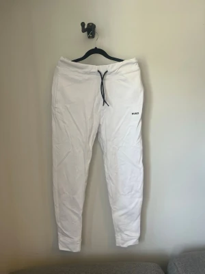 Vita mjukisbyxor från Hugo - Sprillans nya vita mjukisbyxor från Hugo med svarta snören och diskret logga på ena benet. Byxorna har en slim fit-modell och är perfekta för en chill och avslappnad stil. Tillverkade i mjukt material för extra komfort. Storlek S, skick 10/10