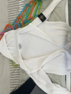 Vit hoodie från Stone Island - Säljer en vit ribbstickad hoodie från Stone Island med dragkedja framtill och klassisk huva. Tröjan har den ikoniska Stone Island-loggan på ärmen och är tillverkad i ett mjukt, stretchigt material. Perfekt för en clean och stilren look.