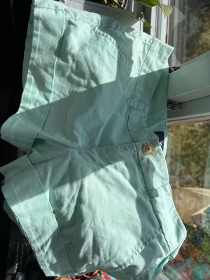 Mintgröna shorts i bomull - Snygga mintgröna shorts med klassisk passform och fickor både fram och bak. Stängs med knapp och dragkedja. Perfekta för varma dagar och har en fräsch, ljus färg som sticker ut.