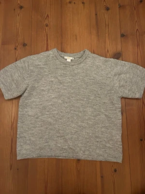 Grå stickad tröja från Gina Tricot - En enkel och stilren grå stickad tröja från Gina Tricot. Tröjan har korta ärmar, rund halsringning och är gjord i ett mjukt stickat material.