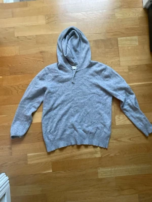 Ljusgrå hoodie från Soyaconcept - Mysig ljusgrå hoodie från Sayless i mjukt stickat material. Klassisk modell med huva och ribbade muddar vid ärmslut och nederkant. Perfekt för en avslappnad och chill stil. En defekt vid luvan, dock inget man märker av och den är möjlig att sy