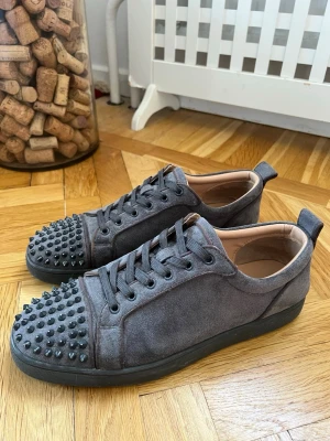 Gråa sneakers med nitar från Louboutin - Ett par feta gråa Christian Louboutin i storlek 44. Dom har lite tecken på användning på sulorna (visas på bilden). Skriv för funderingar.