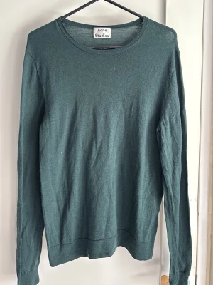 Mörkgrön tröja från Acne Studios - Snygg mörkgrön långärmad tröja från Acne Studios. Tröjan har rund halsringning och är tillverkad i ett tunt, mjukt material som känns skönt mot huden. Perfekt för lager-på-lager och enkel att matcha med jeans eller kjol.