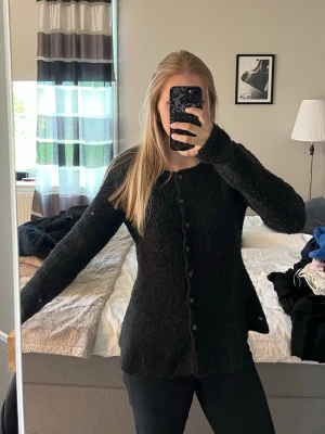 Svart kofta från H&M - Mysig svart kofta från H&M i storlek M. Koftan är stickad med en fluffig struktur, har rund halsringning och knäpps med svarta knappar framtill. 