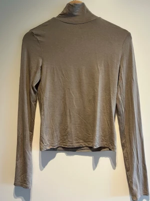 Beige polotopp med lång ärm - Snygg beige polotopp med lång ärm och tight passform. Passar till både vardags men även att klä upp. Tunn och mjuk i materialet. Enkel och stilren design utan mönster eller detaljer.