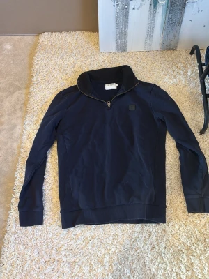 Mörkblå half-zip tröja Les Deux - Mörkblå tröja från Les Deux med halv dragkedja och hög krage. Tillverkad i mjukt material med ribbade muddar vid ärmslut och nederkant. Enkel och stilren design med liten logotyp på bröstet. Perfekt för en avslappnad men snygg look.