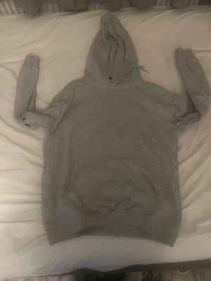 Grå hoodie  Relaxed Fit - En basic grå hoodie från irelaxed fit. Hoodien har huva med dragsko och en stor magficka framtill. Perfekt för en chill och avslappnad stil. Tillverkad i mjukt material som känns skönt mot huden.
