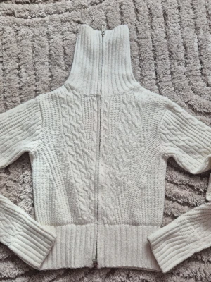 Cremevit stickad kofta/tröja från nelly med dragkedja  - Vit kabelstickad kofta/tröja från Nelly i storlek xs. Är i jätte bra skick och har inga skador. Jätte skön och inte för varm eller för kall. Har ochså dubbel dragkedja. Säljer då den tyvärr är dör liten på mig. Skriv järna om prisförslag eller funderingar ❤️