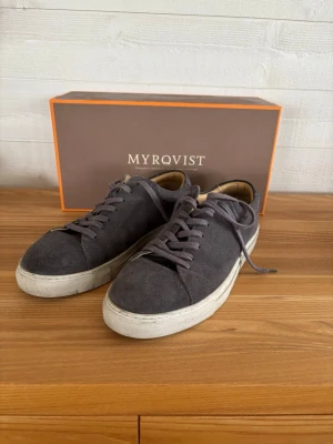 Myrqvist grå mocka sneakers - Snygga sneakers från Myrqvist i grå mocka med vita sulor och matchande grå skosnören. Klassisk låg modell med stilren design och bekväm passform. Perfekta för dig som gillar en clean och tidlös look.