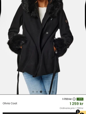 Kapppa ifrån Hollie’s - Stilren svart kappa från Hollie’s Olivia med fuskpälsdetaljer. Kappan är använd 