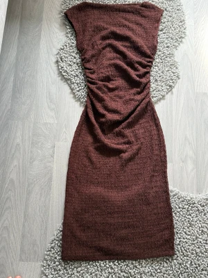 Vinröd strukturerad långklänning - Säljer en vinröd långklänning med strukturerat tyg och rynkade detaljer längs midjan. Klänningen har en enkel, ärmlös design och en smickrande passform. Väldigt classy och elegant