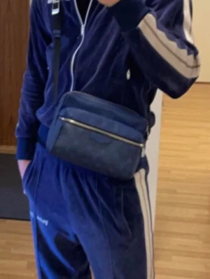 Blå axelväska från Louis Vuitton - Såklart äkta, Låda samt kvitto medkommer det är  en snygg blå axelväska från Louis Vuitton med justerbar rem och diskret monogrammönster. Väskan har en rektangulär form, silverfärgad dragkedja och är tillverkad i canvas med läderdetaljer. Perfekt för dig som vill ha en stilren och exklusiv accessoar.