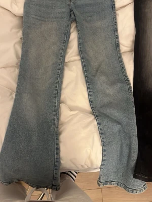 lågmidjad bootcut ljusblå jeans med brodyr - Säljer ett par ljusblå bootcut jeans med snygg broderad detalj på bakfickorna. Jeansen har klassisk femficksdesign och är tillverkade i denim med lätt tvättad look. 