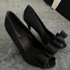 Svarta klackar med rosett - Snygga svarta pumps från Graceland i mycket bra skick. De har en elegant rosett framtill och en spetsig tå. Perfekta för festliga tillfällen! Klacken ger en fin höjd och de är bekväma att gå i.