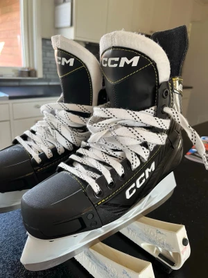 Svarta CCM hockeyskridskor - Säljer ett par svarta CCM skridskor med vita snören och vita detaljer. Skridskorna har robust konstruktion, svart och vit design med gula sömmar och skyddande tunga. Perfekta för hockey eller allmän åkning på is. Snygg och sportig look!                                                                     De är i storlek 42 och är nästan oanvända