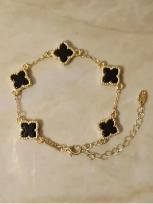 Guldfärgat armband med svarta klöver✨ - Snyggt armband i guldfärg med svarta klöverformade detaljer. Armbandet har en tunn kedja och dekorativa kanter runt klöverna. Justerbar längd med karbinlås och liten bricka vid låset✨