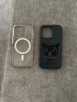 Två mobilskal till iPhone - Säljer två mobilskal till iPhone. Ett transparent skal med MagSafe-ring i vitt, tillverkat i plast. Det andra är svart med en broderad panter och blå ögon på baksidan, gjort i konstläder. Båda skyddar mobilen och har snygg design.