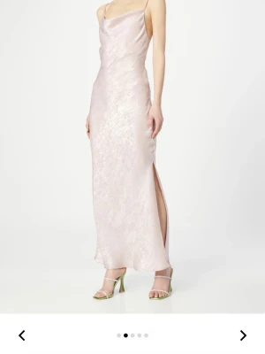 Ljusrosa balklänning i satin -  ljusrosa långklänning/balklänning i skimrande satin med smala axelband och öppen rygg med snörning. Klänningen har en slits på sidan och en mjukt draperad urringning framtill. Använd en gång. Från Vila