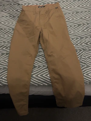 Beiga chinos från Vans - Snygga beiga chinos från Vans med klassisk rak passform och bälteshällor. Tillverkade i ett slitstarkt bomullsmaterial som ger en clean och stilren look. Perfekta för dig som gillar enkel och tidlös stil.