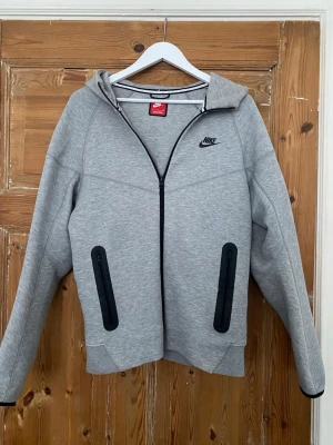 Grå Nike tech  - Säljer denna sköna Nike tech koftan kommer i perfekt skick och i storlek S. Kom gärna fram med bud !