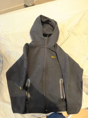 Svarta NOCTA mjukisbyxor från Nike - Säljer ett par svarta mjukisbyxor från Nike NOCTA-kollektionen. Byxorna har gul NOCTA-logga på benet och gul Nike Swoosh på höften. De har dragsko i midjan och dragkedjeförsedda fickor med svarta detaljer. Perfekta för en chill och sportig look.