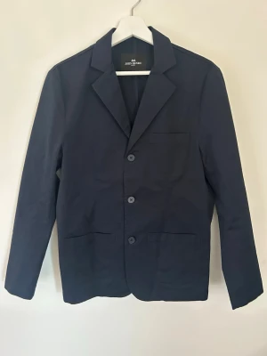 Mörkblå overshirt från John Henric - Stilren mörkblå overshirt från John Henric med klassisk krage och tre knappar framtill. Jackan har två stora fickor nertill och en bröstficka. Tillverkad i ett slätt tyg som ger en clean look och passar perfekt till lager-på-lager-stil. Den är endast använd en gång kan tänka mig sänka pris vid snabb affär🤝