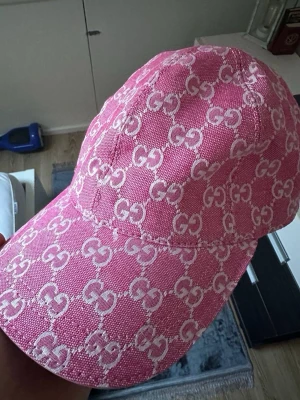 Rosa keps med GG-mönster - Säljer en rosa GG-mönster i vitt över hela kepsen. Kepsen har böjd skärm och ett litet guldfärgat GG-emblem framtill. Storlek M 58cm