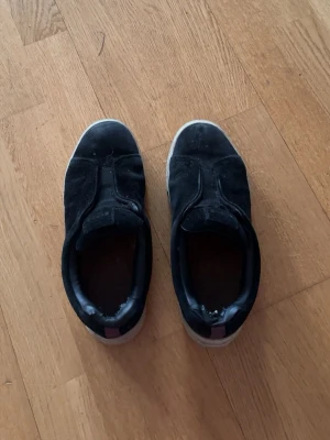 Svarta eytys  - Säljer ett par svarta eytys. Skorna har en enkel och stilren design utan snörning och är tillverkade i mockaliknande material. Passar perfekt till en avslappnad och trendig look.
