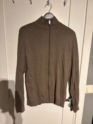 Brun ziptröja  - Säljer en brun ziptröja med hög krage och hel dragkedja framtill. Tröjan är tillverkad i ett mjukt, tunt material och har långa ärmar samt ribbade muddar vid ärmslut och nederkant. Perfekt för lager på lager och enkel att matcha.