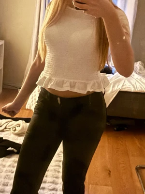 Vit smockad topp med volangkant - Supersöt vit topp med smockad kropp och volangkant nedtill. Kortärmad modell med rund halsringning och lätt croppad passform. Perfekt att styla med höga jeans eller kjol för en fräsch look. Den är i storlek 146/152 men skulle säga att den passar xs-S också, normaltvis har jag storlek S. Pris kan diskuteras!