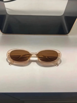 Ovala solglasögon med beige bågar - Snygga solglasögon med transparenta beige bågar och bruna, ovala glas. Perfekta för att höja din stil på sommaren. Lätta och bekväma att bära, passar till de flesta outfits.