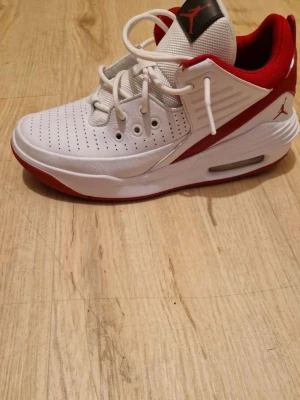 Vita och röda Air Jordan sneakers - Säljer ett par snygga Air Jordan sneakers i vitt och rött med perforerad tå, röda detaljer och klassisk Jumpman-logga på plösen och hälen. Skorna har en chunky sula med synlig luftdämpning och vita skosnören. Perfekta för dig som gillar streetwear och sportig stil.