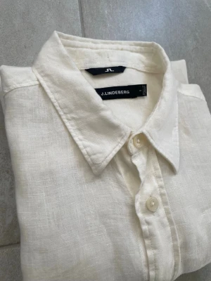 Vit linneskjorta från J.Lindeberg - Snygg vit skjorta från J.Lindeberg i svalt linne. Klassisk krage, korta ärmar och knappar framtill. Perfekt för varma dagar när du vill ha en clean och stilren look.                        Mått 📏 Längd från axel: 72cm Axelbredd: 42cm Skador 🔧: Inga  Storlek 🧍: M (Står S men passar som M)  Jag kan förhandla mig till lägre pris.🙋💵 Om du har några frågor, vänligen skriv till mig 🤗