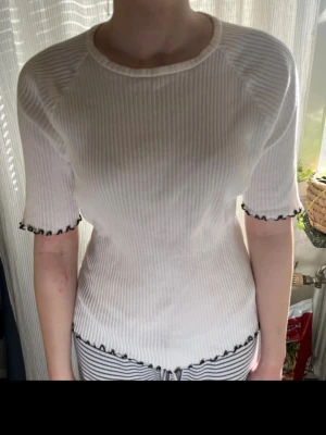 Vit ribbad topp med svarta volangkanter från weekday  - Supersöt vit ribbad topp med korta ärmar och svarta volangdetaljer vid ärmslut och nederkant. Som ny! 