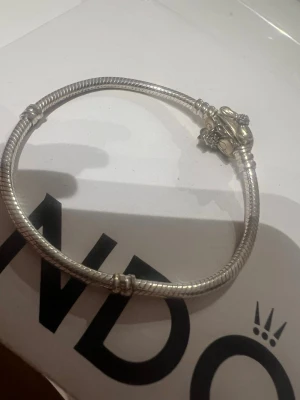 Pandora silverarmband med krona - Snyggt silverfärgat armband från Pandora med en detaljerad krona som lås. Armbandet har en klassisk orm-länk design och är perfekt för att addera egna berlocker. Passar dig som gillar stilrena och tidlösa accessoarer.