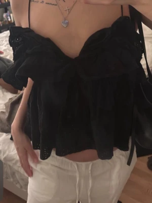 Svart offshoulder blus med volang - Säljer en svart offshoulder blus med tunna axelband och stora volanger framtill. Blusen har en luftig och loose passform, perfekt för varma dagar. Materialet känns lätt och har fina broderade detaljer längs kanterna.
