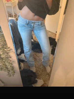 Ljusblå bootcut jeans - Säljer ett par ljusblå bootcut jeans med låg midja och klassisk femficksdesign. Jeansen har en snygg tvätt och stängs med dragkedja och knapp. Perfekta för en avslappnad och trendig look.