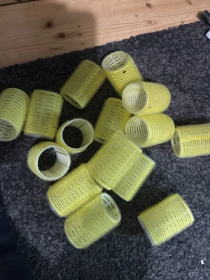 Gula självhäftande hårspolar - Ett gäng gula självhäftande hårspolar i plast, perfekta för att skapa volym och lockar i håret. Spolarna har en cylinderform och är lätta att använda utan hårnålar tack vare det greppiga materialet. Passar både kort och långt hår.