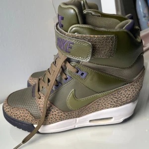 Nike wedges med leopardmönster - Säljer ett par unika Nike Air sneakers i olivgrönt med leopardmönstrade detaljer och lila accenter. Skorna har hög modell med kardborreband, snörning och vit sula med synlig luftdämpning. Perfekta för dig som vill sticka ut med din stil. Pris går att diskuteras.😊