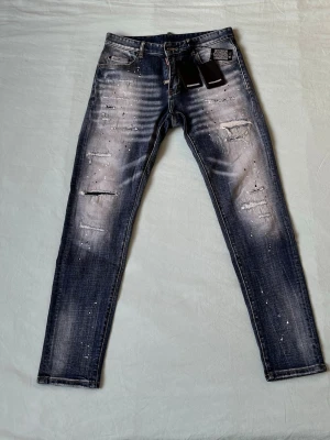 Mörkblå distressed jeans Dsquared2 - Snygga mörkblå jeans från Dsquared2 med slitningar, blekta partier och färgstänk. Klassisk femficksmodell med smal passform och låg midja. Perfekta för dig som gillar en edgy streetstil.
