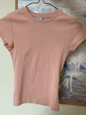 Ljusrosa t-shirt från Bershka - En enkel och stilren ljusrosa t-shirt från Bershka. Modellen har rund halsringning och korta ärmar. Tillverkad i mjuk bomull som känns skön mot huden. Perfekt att matcha med jeans eller kjol för en clean look.
