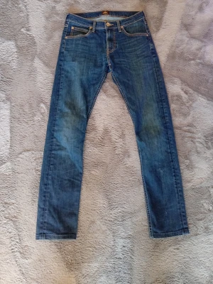 Jeans - Säljer ett par klassiska blå jeans med raka ben och kontrastsömmar. Jeansen har fem fickor, bälteshällor och knappgylf. Materialet är denim i bomull och passformen är normal. Perfekta till en avslappnad stil.