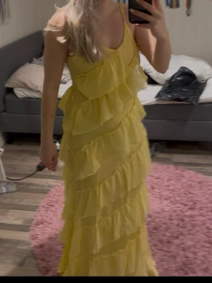 Gul långklänning med volanger - Säljer en superfin gul långklänning med flera lager volanger. Klänningen har ärmlös design och djup v-ringning, perfekt för sommarens alla tillfällen. Tillverkad i ett lätt och luftigt material som ger en flowy känsla.